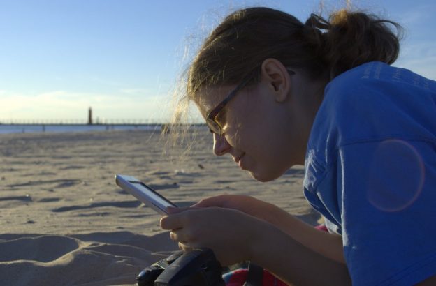 nainen lukee e-kirjaa rannalla lukulaitteesta. Kuva: Michael Mol.