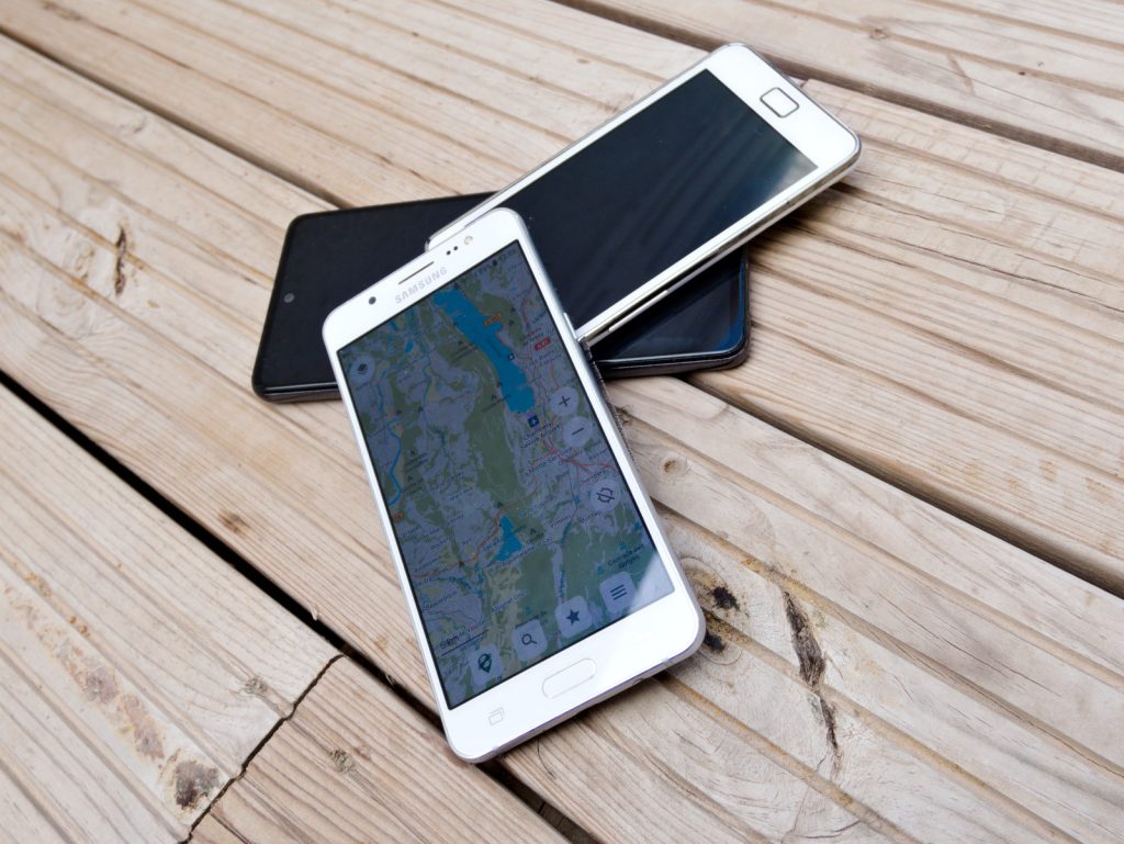 kolme puhelinta, joista yhden näytöllä kartta.